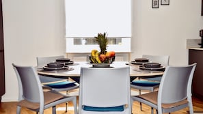 Un espace repas moderne avec une table ronde, six chaises et un saladier à fruits.