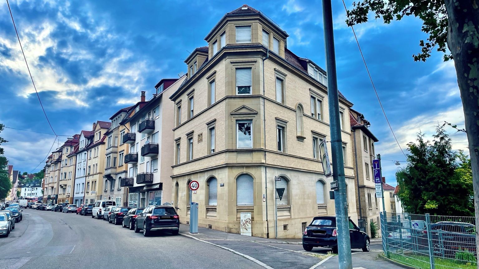 A street view with a row of parked cars, a building with a corner entrance, and a clear sky.