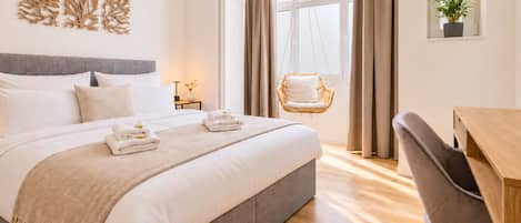 A hotel room with a bed, a chair, a desk, and a window with curtains.