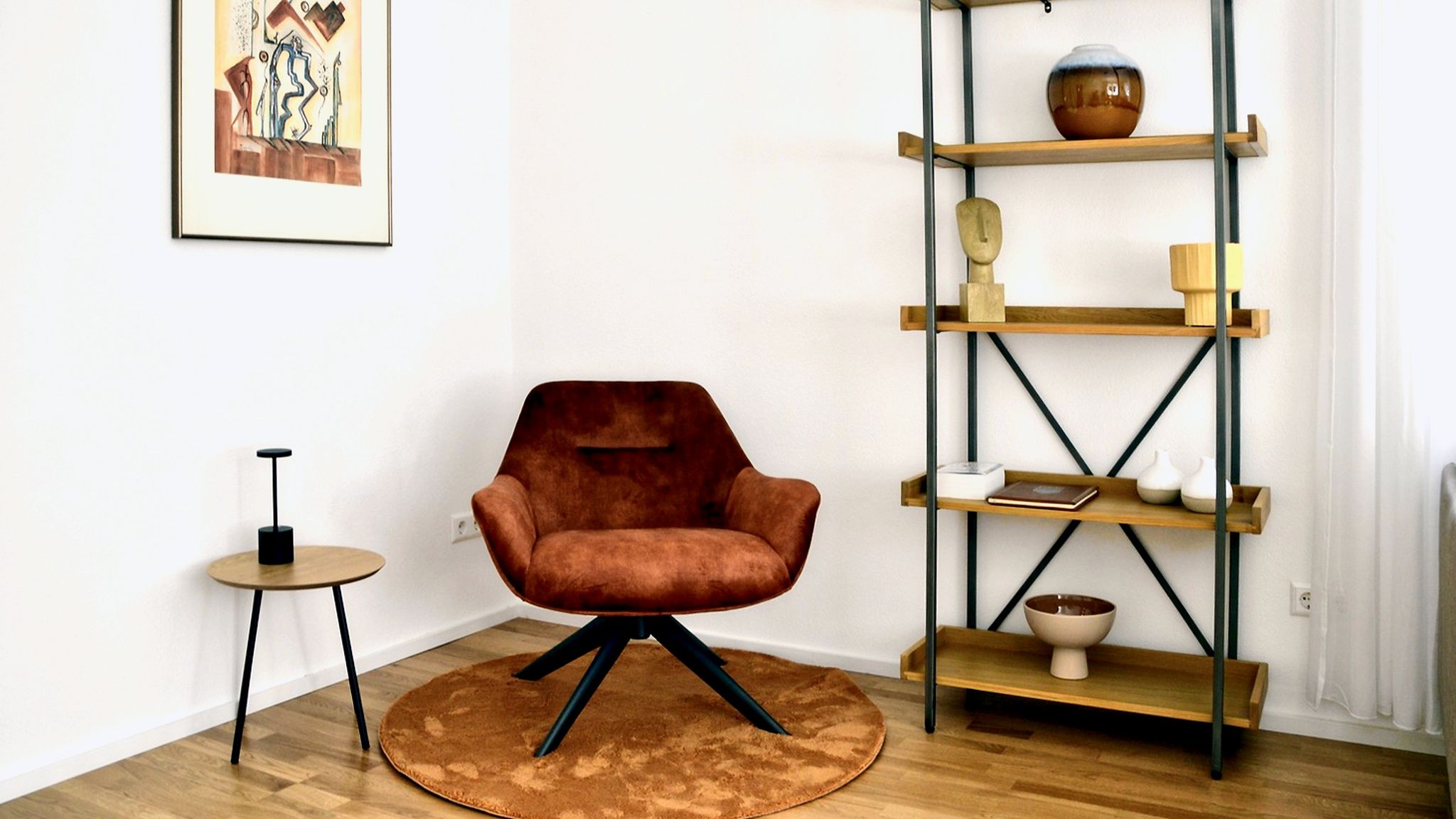 Um quarto com uma poltrona marrom, um tapete redondo, uma mesa pequena e uma estante de madeira com diversos objetos.