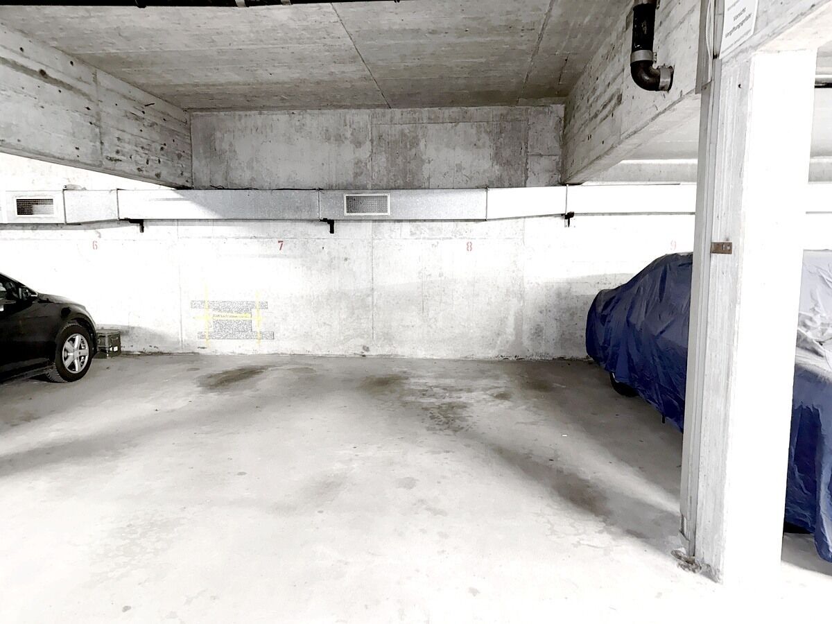 A parking garage with concrete walls, numbered parking spaces, and a car parked in one of the spaces.