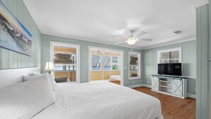 Quarto com uma cama grande, um ventilador de teto, uma TV sobre um suporte de madeira e vista para o exterior pela janela.