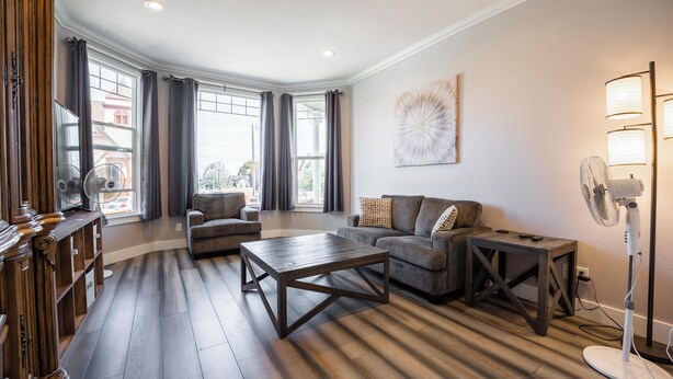 A modern living room with a wooden floor, a sofa, a coffee table, and a standing fan. - Beautiful Victorian Home (Tacoma)