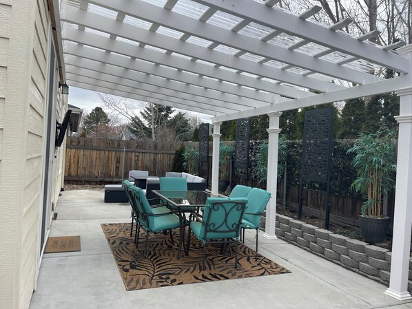 A covered patio with a table and chairs, a zebra-patterned rug, and a wooden fence in the background.