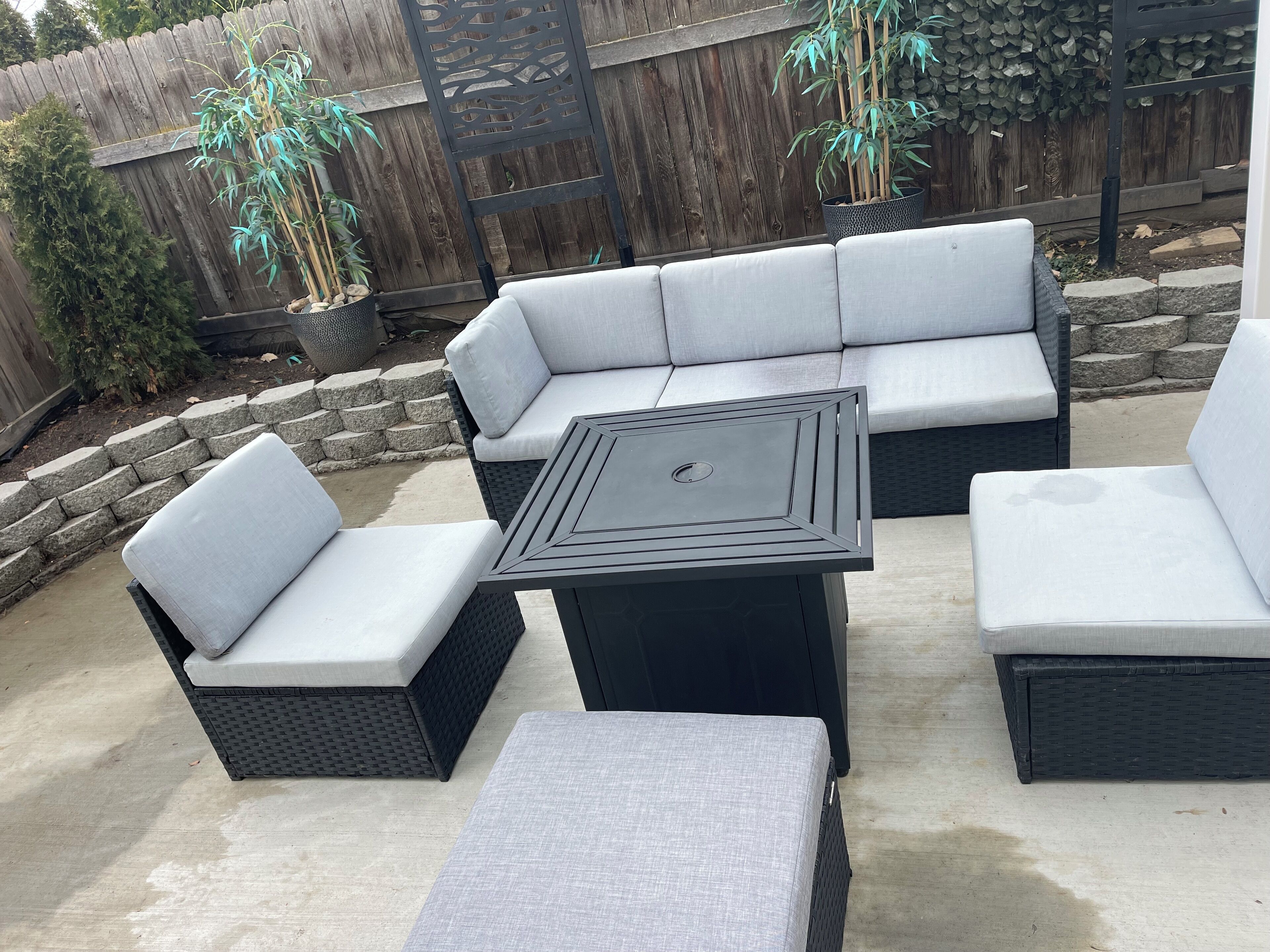Une terrasse extérieure avec un canapé modulable, deux fauteuils rembourrés et une table carrée.