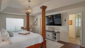 A spacious bedroom with a large bed, a wooden headboard, a television, a desk, and a window with blinds. - Large House, Fireside Hot Tub, King Bed Suite (lakeland)