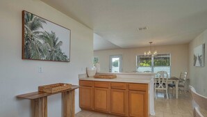 A kitchen with wooden cabinets, a central island, and a dining area with white chairs. - Large House, Fireside Hot Tub, King Bed Suite (lakeland)