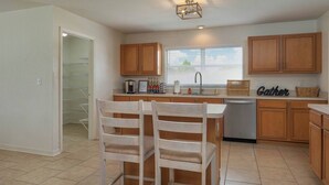 A kitchen with wooden cabinets, a central island with two chairs, a dishwasher, and a window with blinds. - Large House, Fireside Hot Tub, King Bed Suite (lakeland)