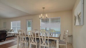 A dining area with a wooden table and white chairs, a chandelier, and a view through large windows. - Large House, Fireside Hot Tub, King Bed Suite (lakeland)