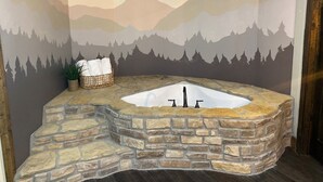 A stone bathtub with a mountain mural backdrop, a basket with towels, and a potted plant. - Whippoorwill Run Cabin — Jasper, AR (Jasper)