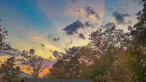 A wooden cabin with a porch and a gravel driveway, surrounded by trees and a sunset in the background. - Whippoorwill Run Cabin — Jasper, AR (Jasper)