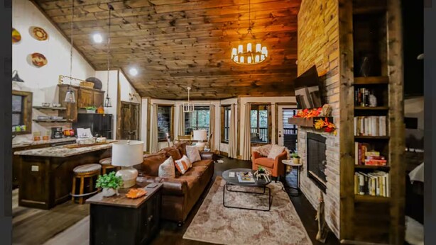 A cozy living room with a fireplace, wooden ceiling, and a stone wall. - Whippoorwill Run Cabin — Jasper, AR (Jasper)