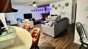 A modern living room with a sofa, armchairs, a dining table, and a kitchen area with a stove.