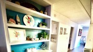 A room with a white cabinet with teal shelves, a small table, and a door leading to another room.