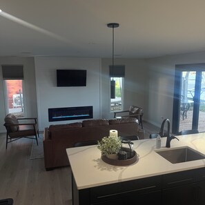 A modern living room with a fireplace, a flat-screen TV, and a dining area with a kitchen island.