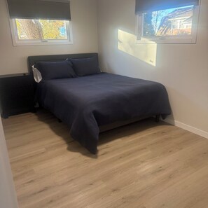 A bedroom with a bed, two windows, and a radiator.