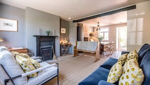A living room with a fireplace, a sofa, a chair, and a dining area. - Key Cottage, Orford (Orford)