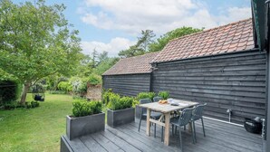 A wooden deck with a table and chairs, surrounded by planters and a garden. - Key Cottage, Orford (Orford)