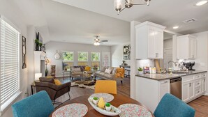 Une cuisine moderne avec des meubles blancs, un îlot central et un coin repas comprenant une table ronde et des chaises bleues.