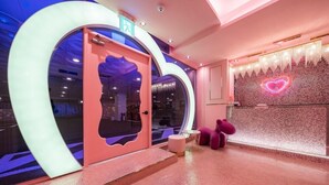 A modern interior with a circular glass door, a heart-shaped neon sign, and pink seating. - JANGYU ALMOND KIDS HOTEL (Gimhae)