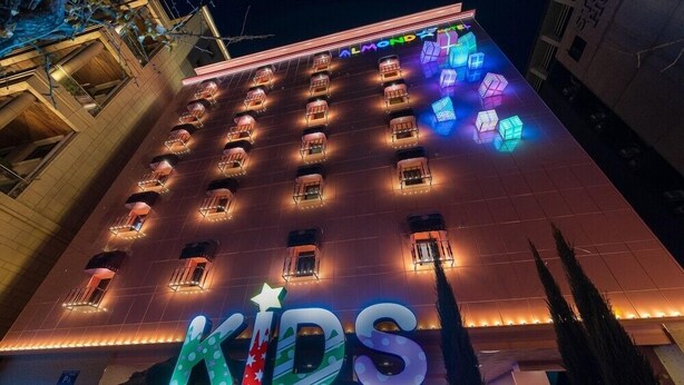 A hotel with a large illuminated 'KIDS' sign at the entrance, multiple balconies, and a modern architectural design. - JANGYU ALMOND KIDS HOTEL (Gimhae)