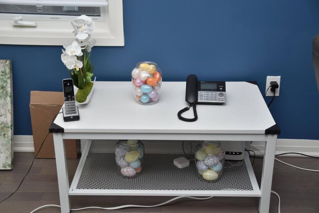 A white desk with a phone, a vase of flowers, and a jar of colorful eggs.