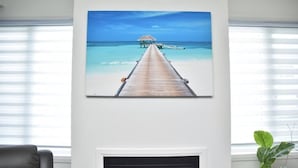 A room with a large painting of a beach scene, a fireplace, and a potted plant. - PARADISE VILLA 8 (Bowmanville)