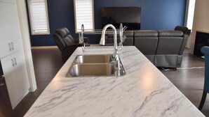 A modern kitchen with a marble countertop, stainless steel sink, and a built-in oven. - PARADISE VILLA 8 (Bowmanville)