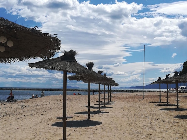 A beach with thatched umbrellas and a clear sky.