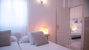 A hotel room with two beds, a nightstand with a lamp, and a door leading to another room.