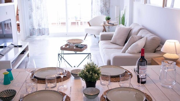 A dining area with a table set for four, a sofa, and a TV in the background.