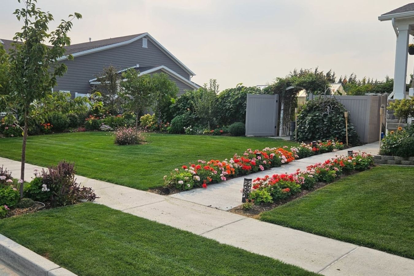 A residential property with a well-maintained lawn, flower beds, and a pathway leading to a covered porch.