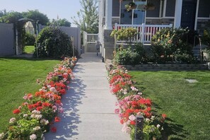A pathway lined with flower beds leading to a building with a white porch and hanging flower baskets.