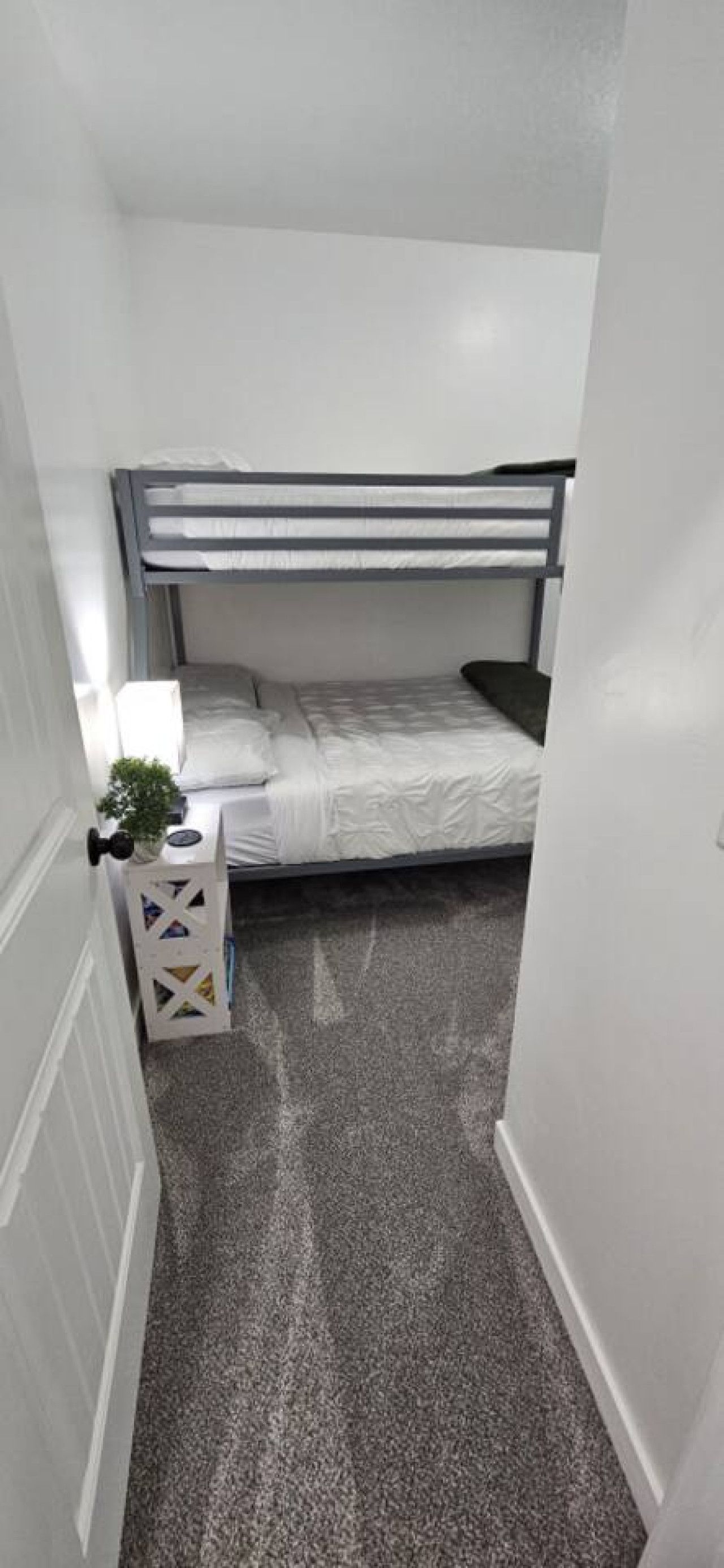 Une petite pièce étroite avec un lit superposé, une petite table de chevet avec une lampe et une boîte décorative.