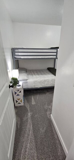 A narrow room with a bunk bed, a small bedside table with a lamp, and a decorative box. - Lehi Oasis | Hot Tub | Firepit | 3D Theatre Room (Lehi)