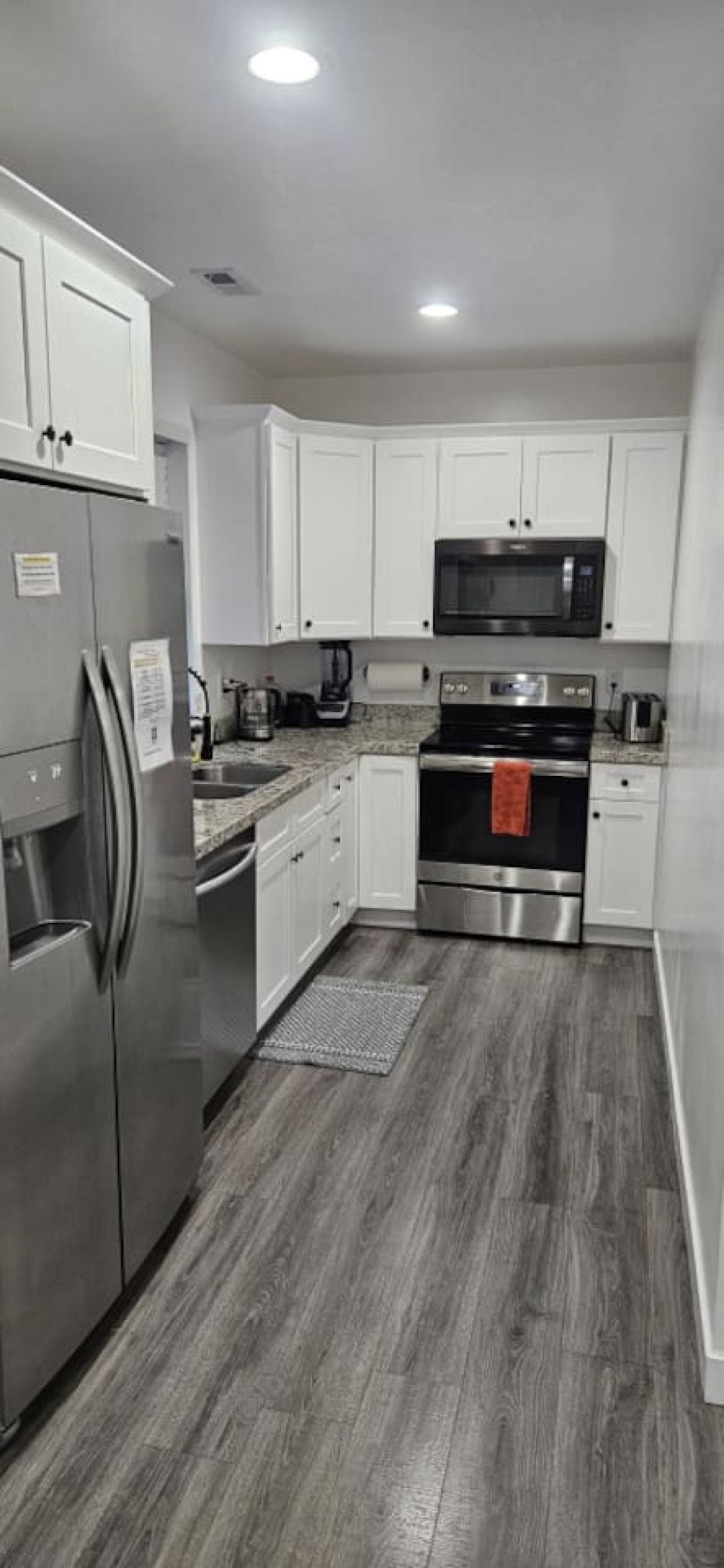 Une cuisine moderne dotée d’appareils électroménagers en acier inoxydable, de meubles blancs et d’un plancher en bois.