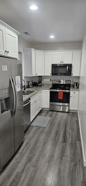 A modern kitchen with stainless steel appliances, white cabinetry, and a wooden floor. - Lehi Oasis | Hot Tub | Firepit | 3D Theatre Room (Lehi)