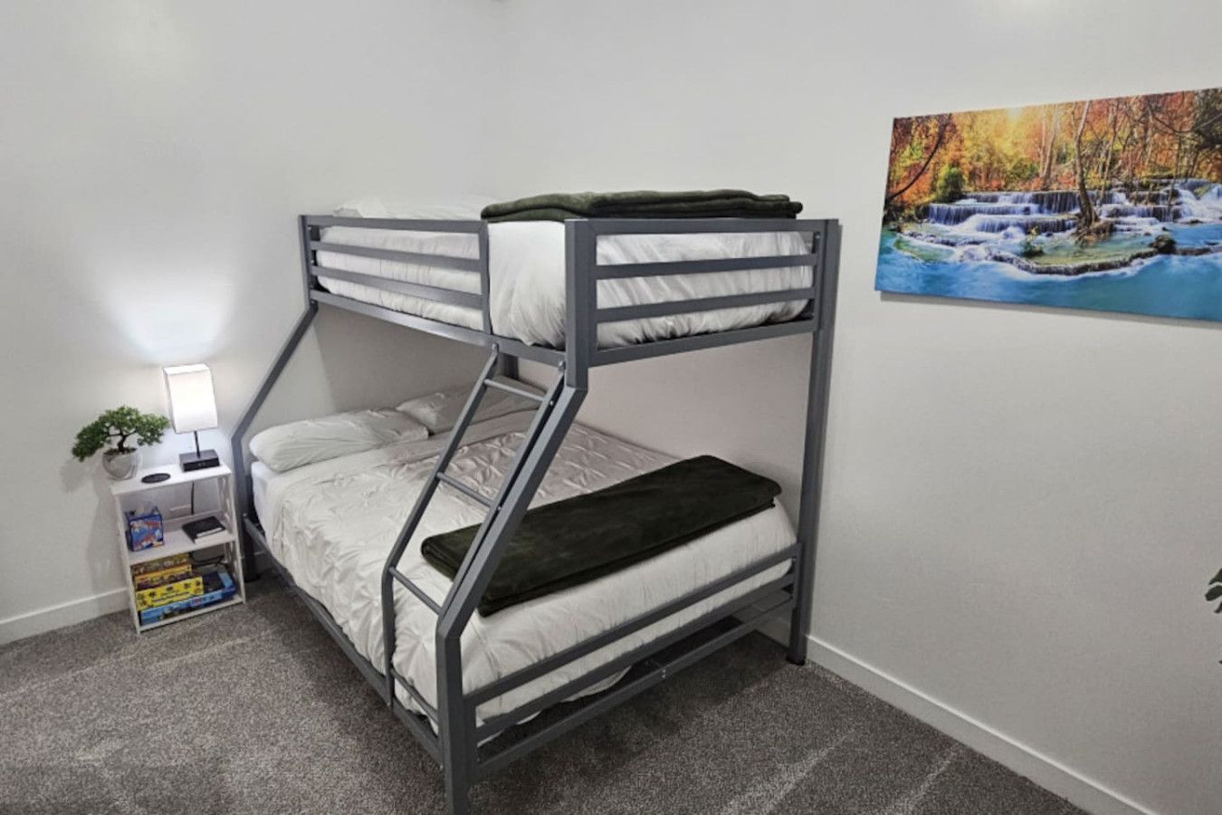 Una cama individual superpuesta con escritorio y silla, una planta pequeña en maceta, y un cuadro en la pared.