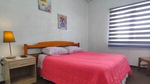 A bedroom with a bed, a nightstand, a lamp, and a window with blinds. - Hospedaje Central Temuco (Temuco)