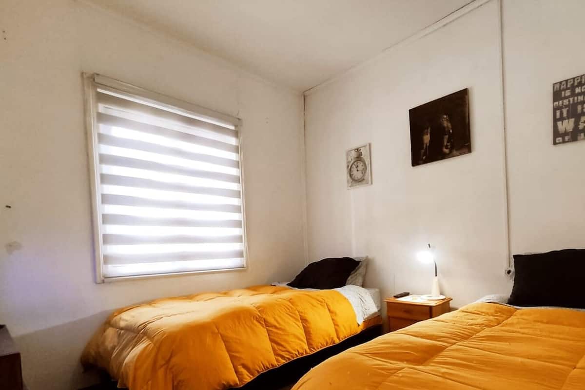A bedroom with two beds, a window with blinds, a bedside lamp, and a wall clock.
