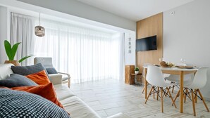 Una sala de estar moderna con un sofá, una mesa de comedor y sillas. Hay un televisor montado en la pared y una planta sobre la mesa.