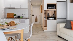 Una cocina moderna con armarios blancos, una mesa de comedor con sillas y un sofá blanco con un cojín naranja.