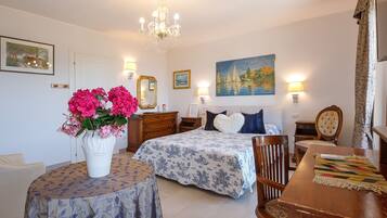 A bedroom with a bed, bedside tables, a chair, a table, a vase with flowers, and wall art.