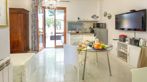 Una cuina moderna amb una taula de menjador preparada per a dues persones, un televisor penjat a la paret i una porta corredissa de vidre que dona a una zona exterior.