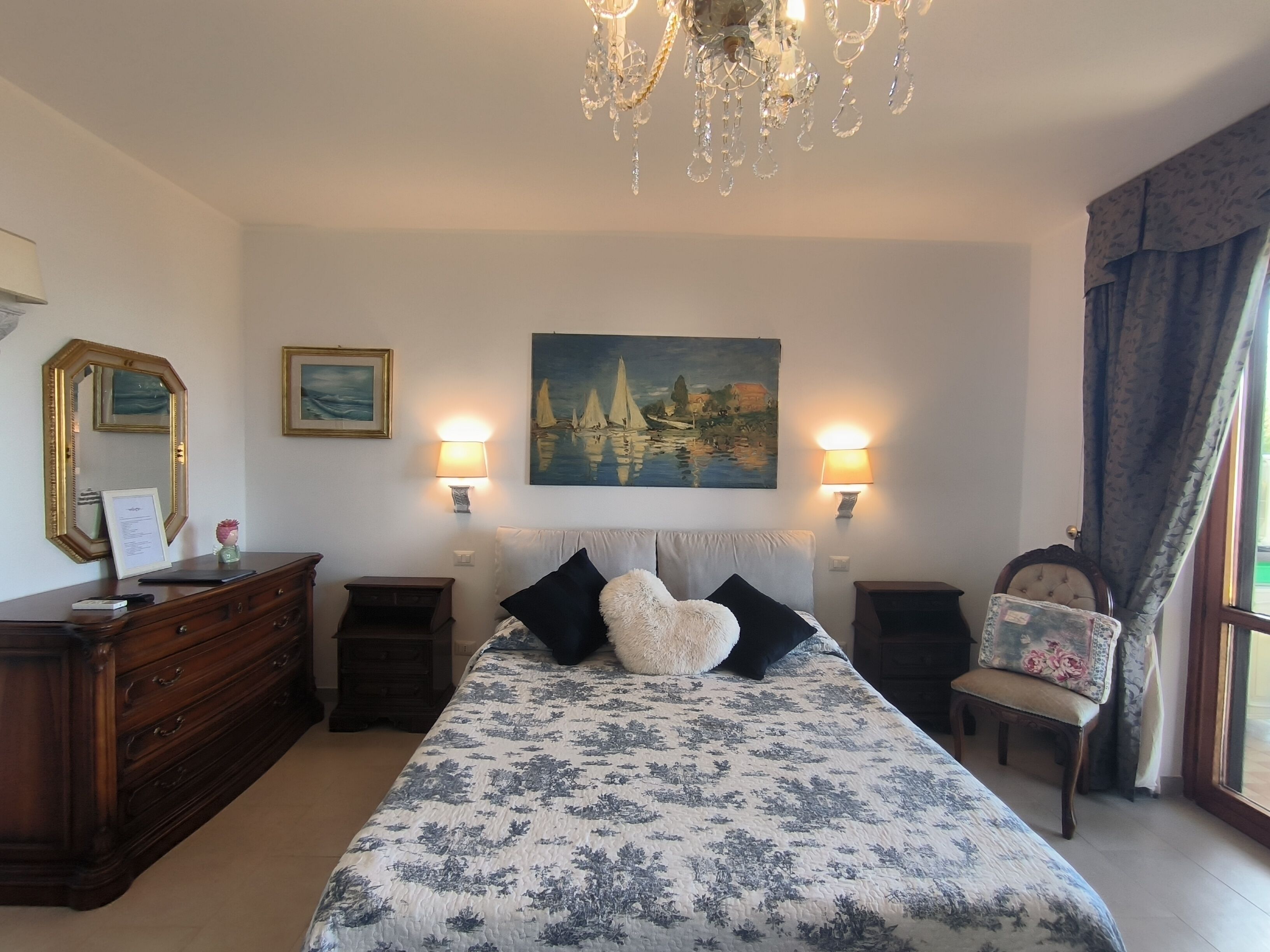 Une chambre à coucher comprenant un lit, une commode, des tables de chevet, un lustre, un tableau et une chaise.