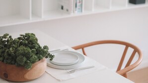 A white dining table with a wooden chair, a small wooden cutting board with a croissant, a potted plant, and a black pendant light. - Deluxe Studio with King size bed, Kitchenette and beach service at Bal Harbour. Beach service included (Bal Harbour)