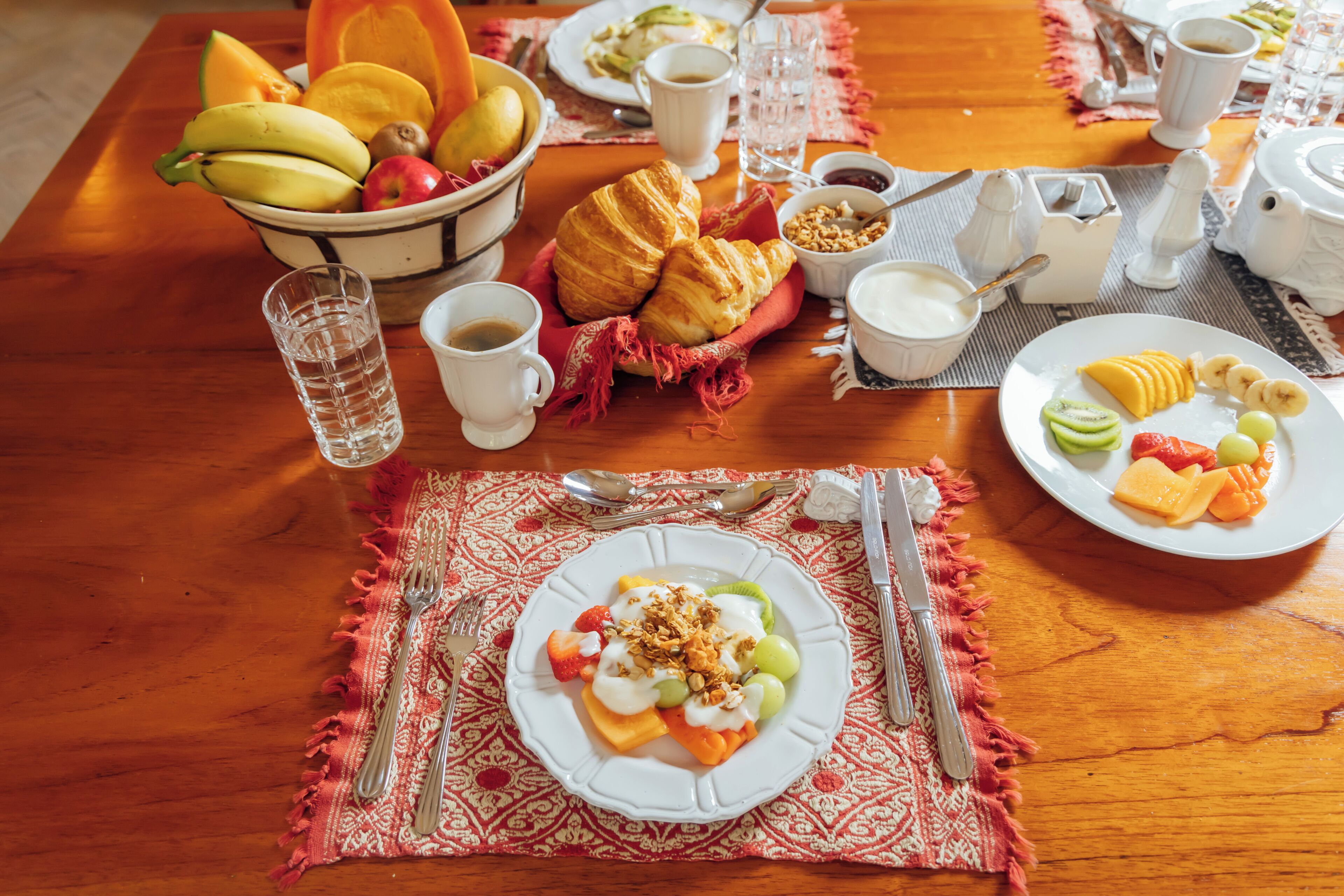 Ett frukostbord med croissanter, frukt och en tallrik med yoghurt och müsli.