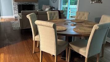 A dining area with a wooden table and chairs, a brick fireplace, and a large window.