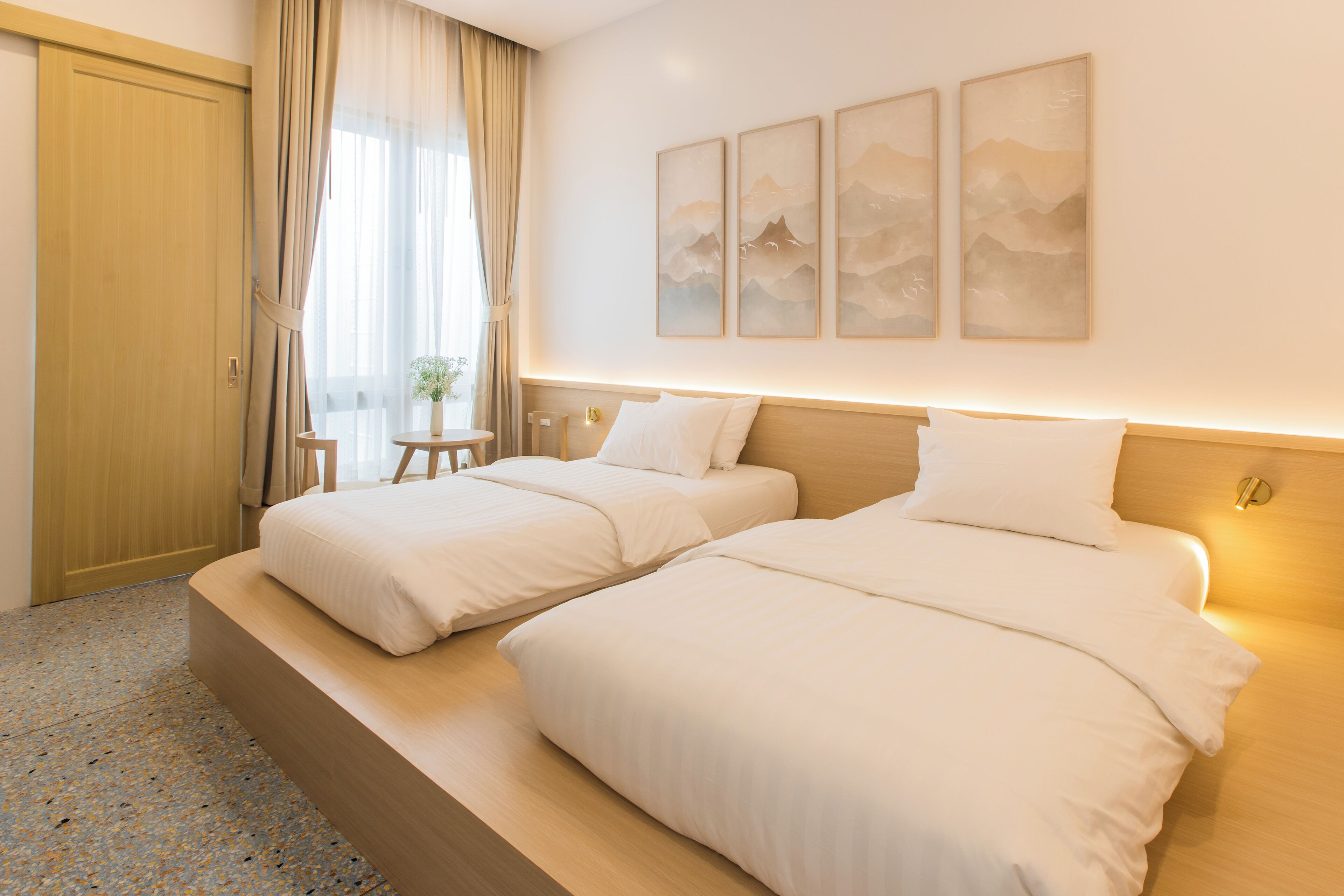 Ein Hotelzimmer mit zwei Betten, einem hölzernen Kopfteil, einem kleinen Tisch mit einer Pflanze und einem Kunstwerk an der Wand.