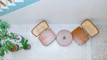 A top-down view of a seating area with a round table and two cushioned chairs, surrounded by potted plants.
